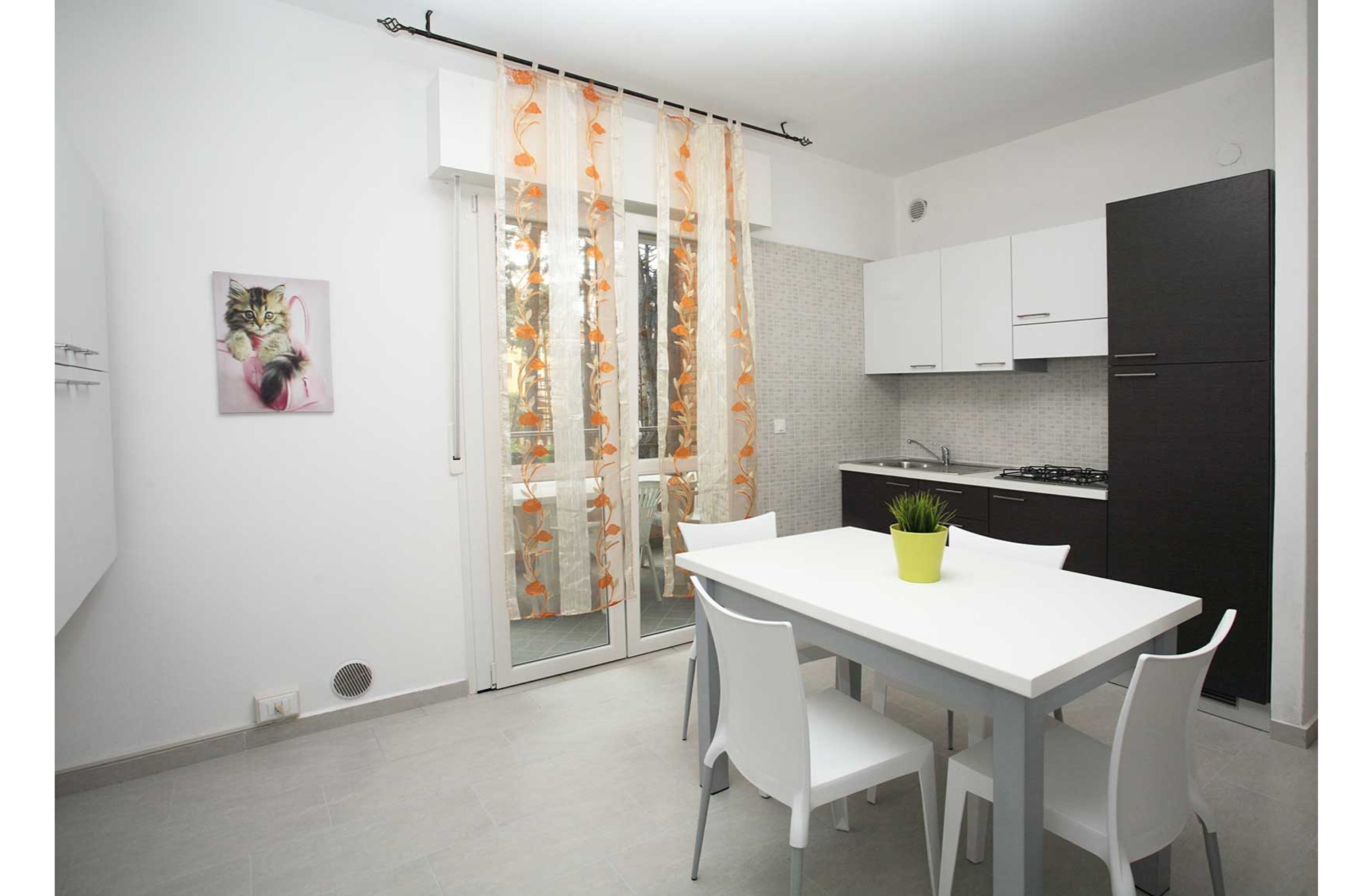 Una cucina moderna con mobili bianchi, un frigorifero nero e un'area pranzo con tavolo e sedie bianche.
