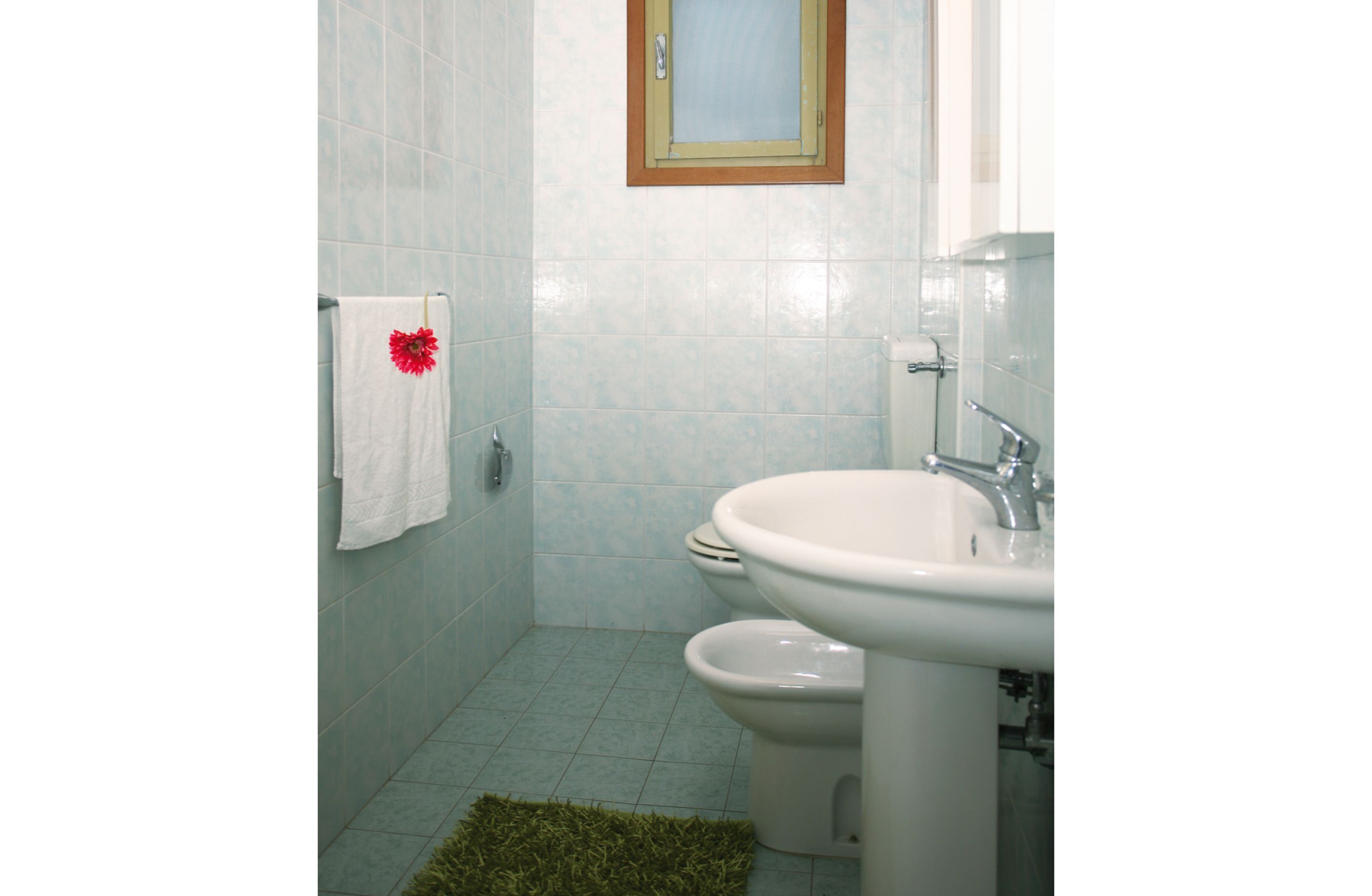 Une salle de bain avec des toilettes, un lavabo et une petite fenêtre située au-dessus du miroir.
