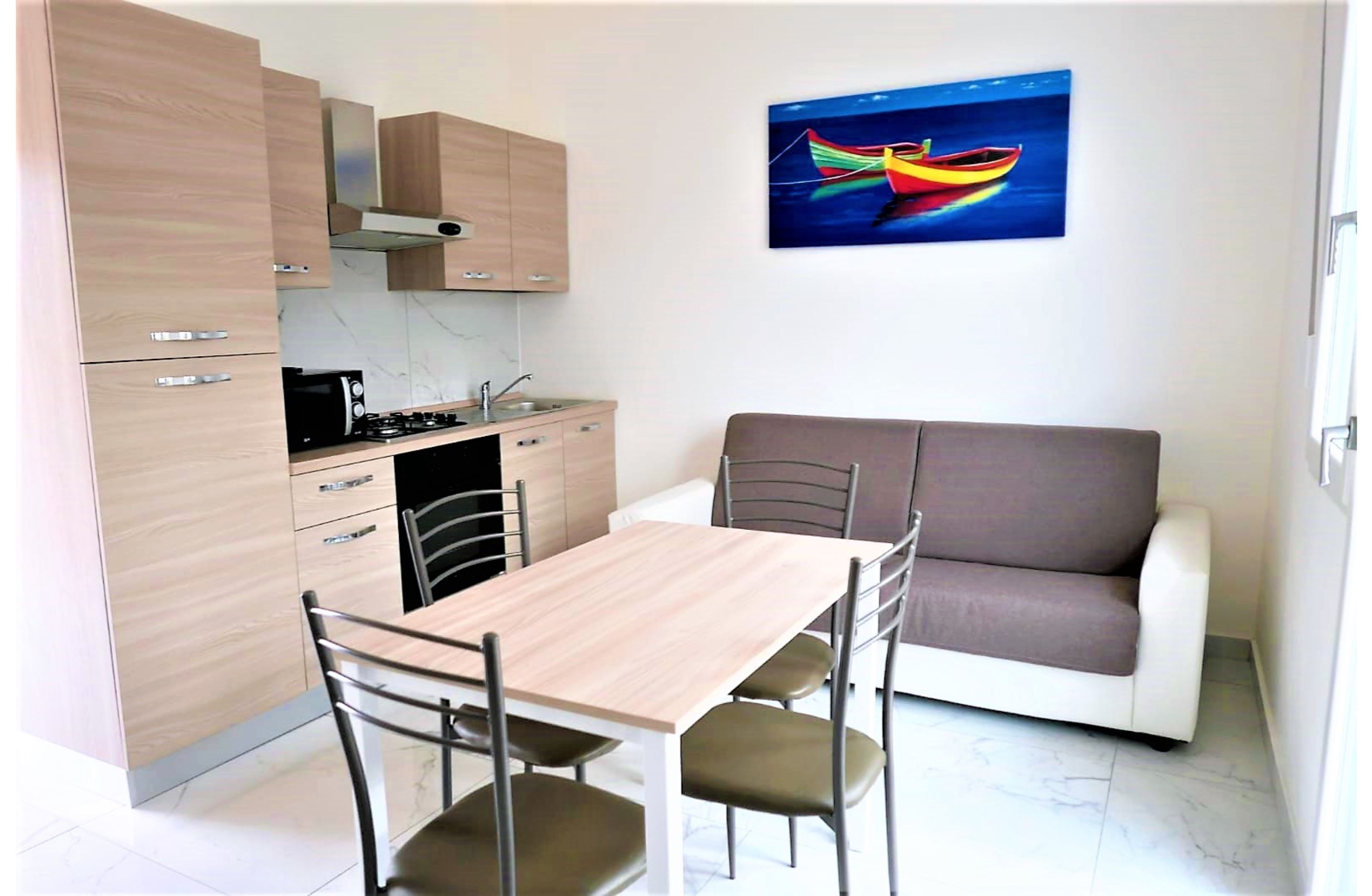 A compact kitchen with a dining area, a sofa, and a painting of a boat on the wall.