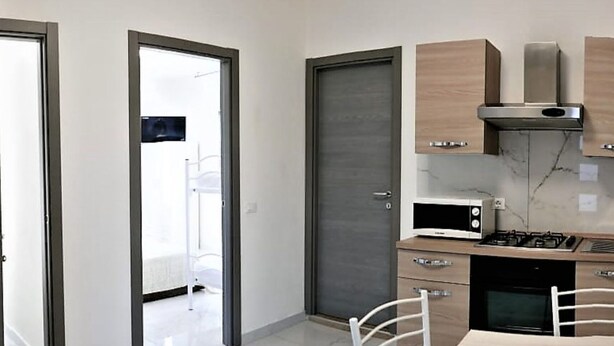 Eine kleine Küche mit Kühlschrank, Mikrowelle, Herd und Spüle. Ein Fernseher ist über dem Kühlschrank angebracht.