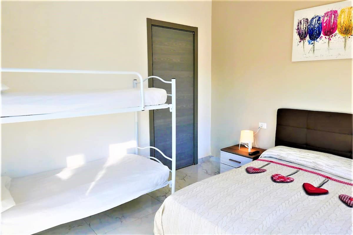Une chambre d’hôtel avec un lit superposé, un lit simple, une table de chevet avec une lampe et une œuvre d’art murale.