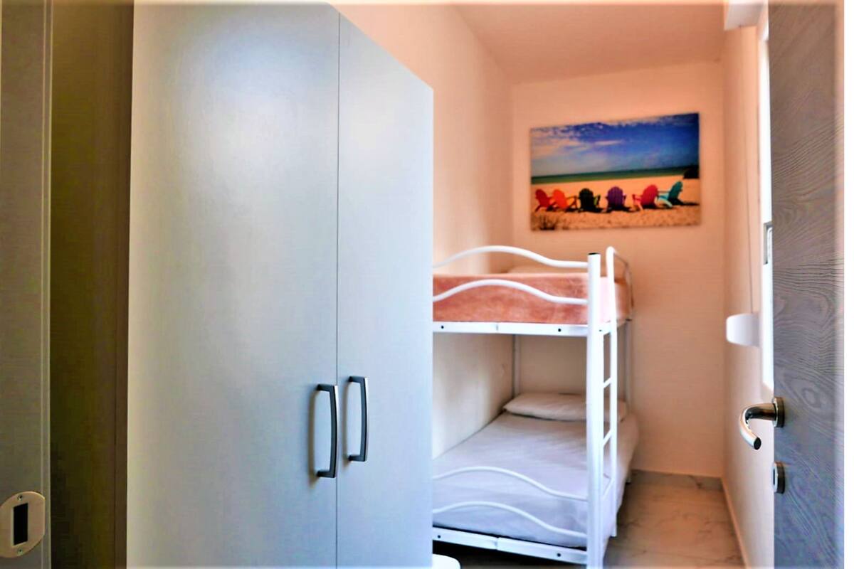 Un lit superposé dans une petite pièce, avec un tableau représentant une scène de plage accroché au mur.
