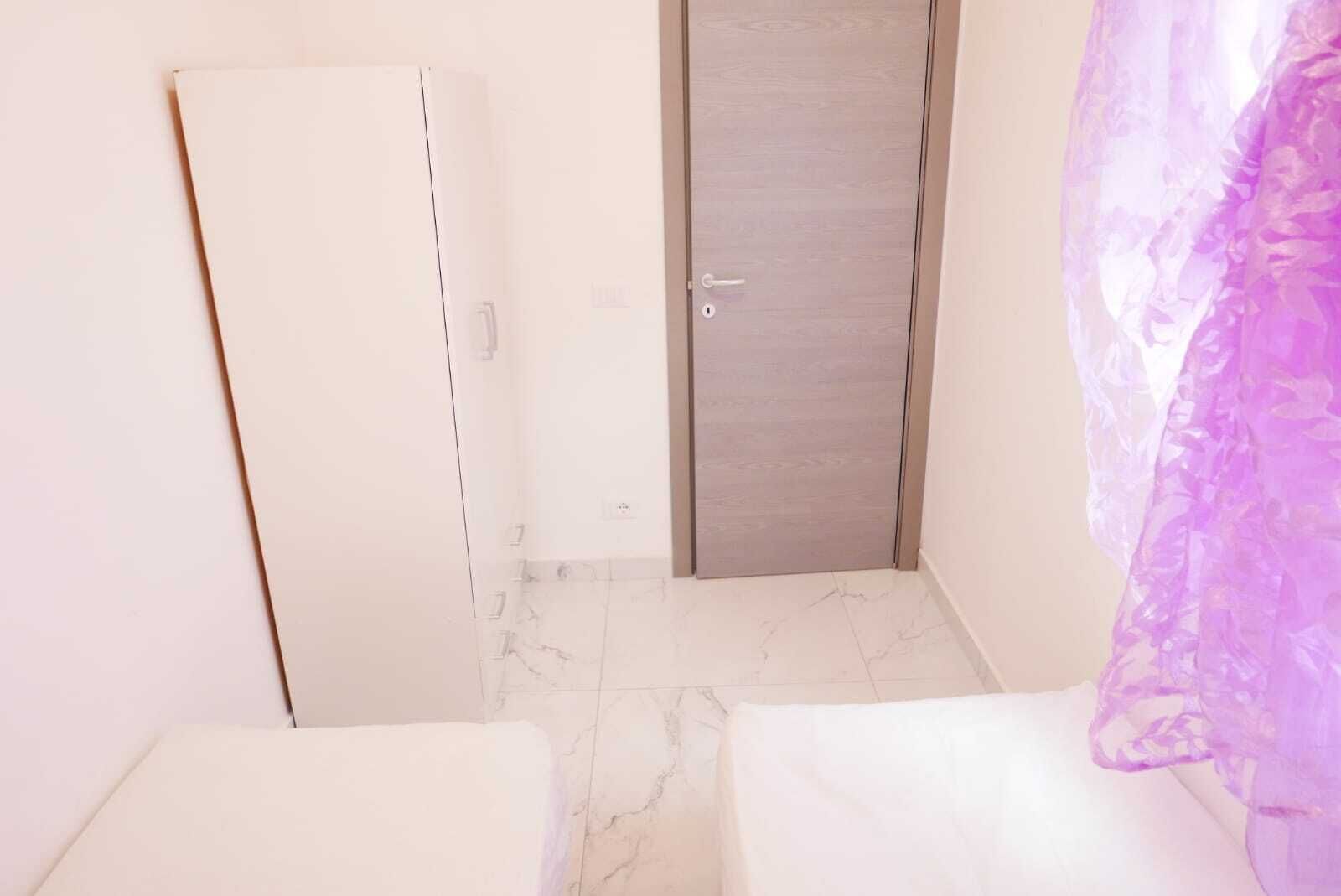 Um quarto pequeno e estreito, com um guarda-roupa branco, uma porta e uma cortina roxa.