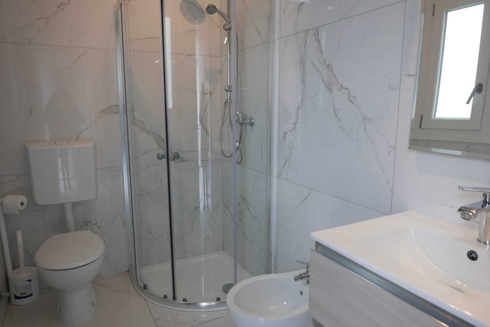 Uma casa de banho com cabine de duche em vidro, sanita e lavatório com espelho.