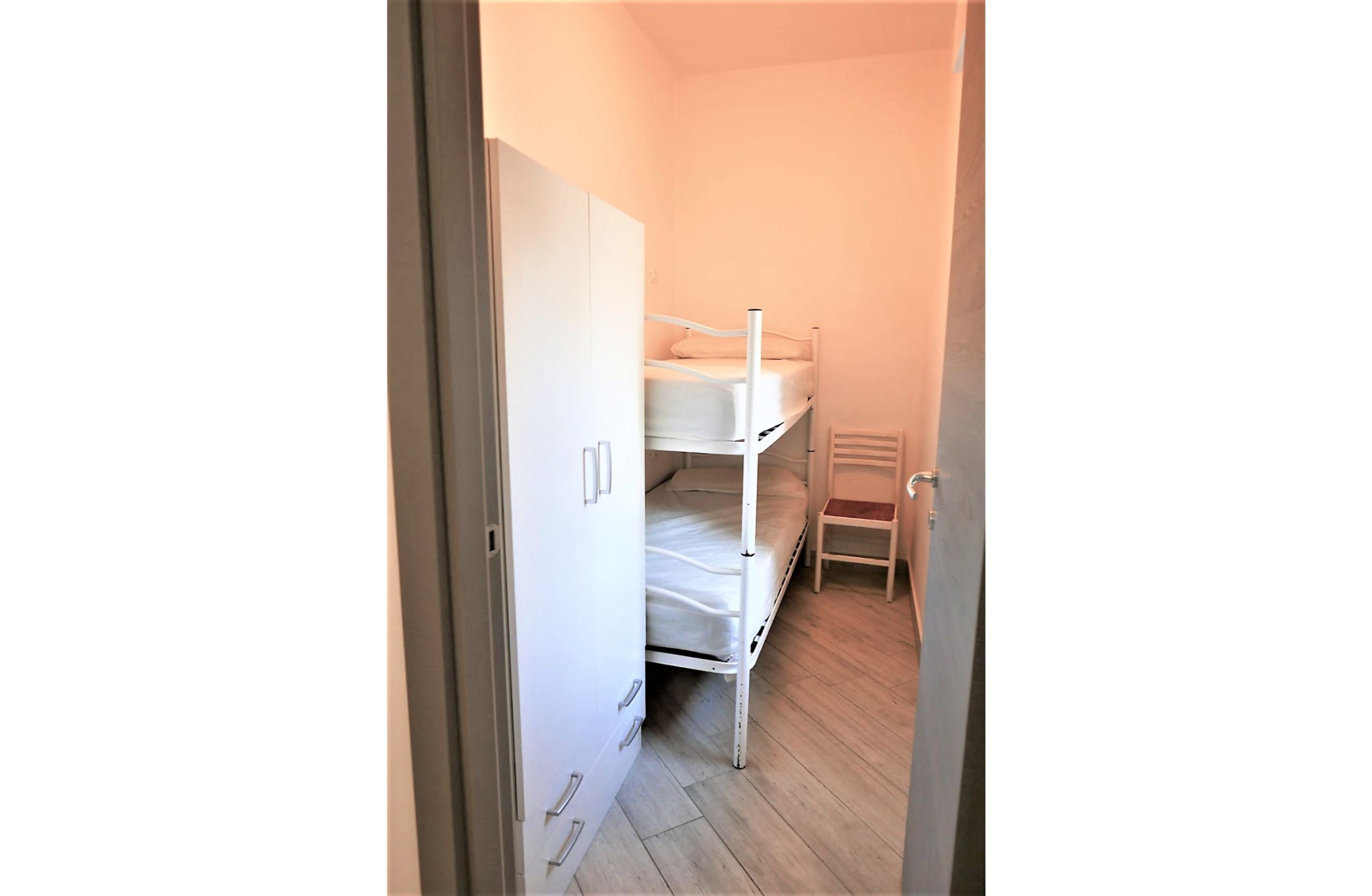 A room with a bunk bed, a wardrobe, and a chair.