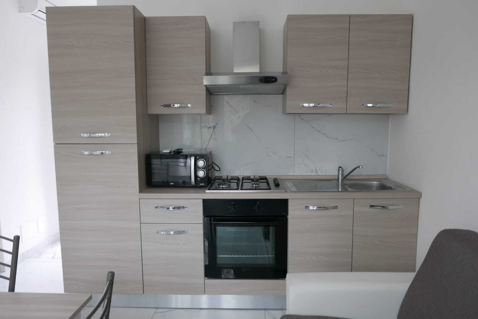 A modern kitchen with light wood cabinets, a built-in microwave, gas stove, sink, and oven.