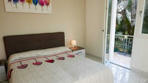 Ein Schlafzimmer mit Bett, Nachttisch, Lampe und Blick ins Freie durch eine Schiebetür.