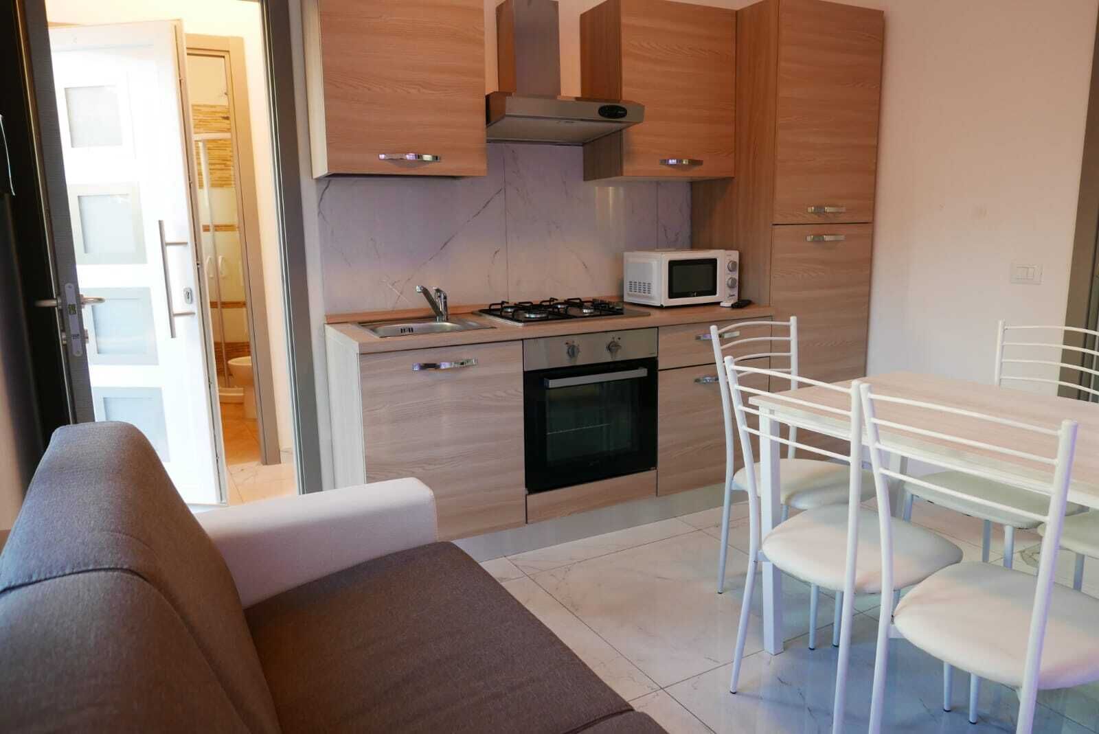 Une cuisine compacte équipée d’un four à micro-ondes, d’une cuisinière, d’un four et de meubles de rangement en bois. On y trouve une table à manger avec des chaises, ainsi qu’un canapé dans le salon attenant.