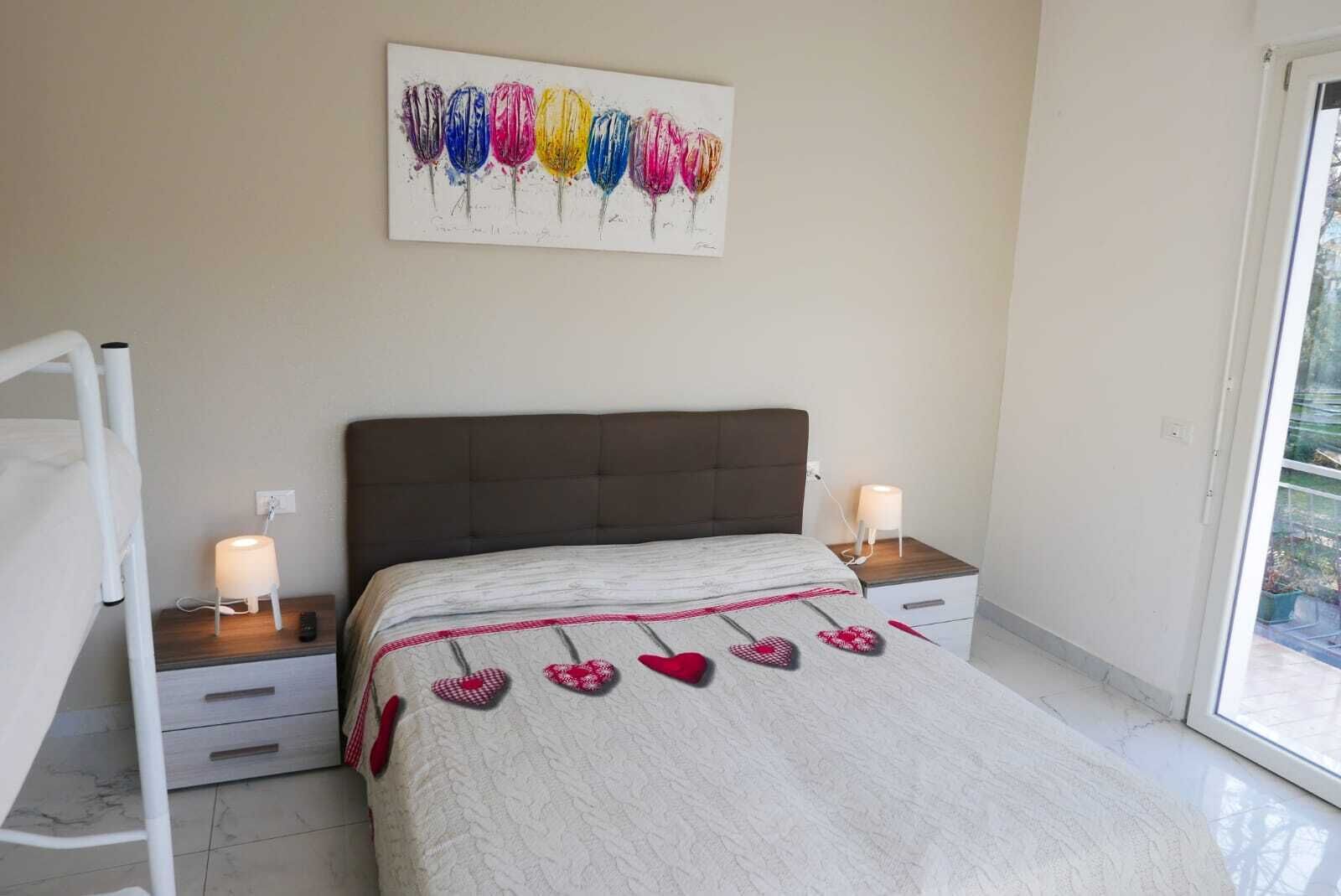 A bedroom with a bed, bedside tables, a nightstand, a wall art piece, and a window.