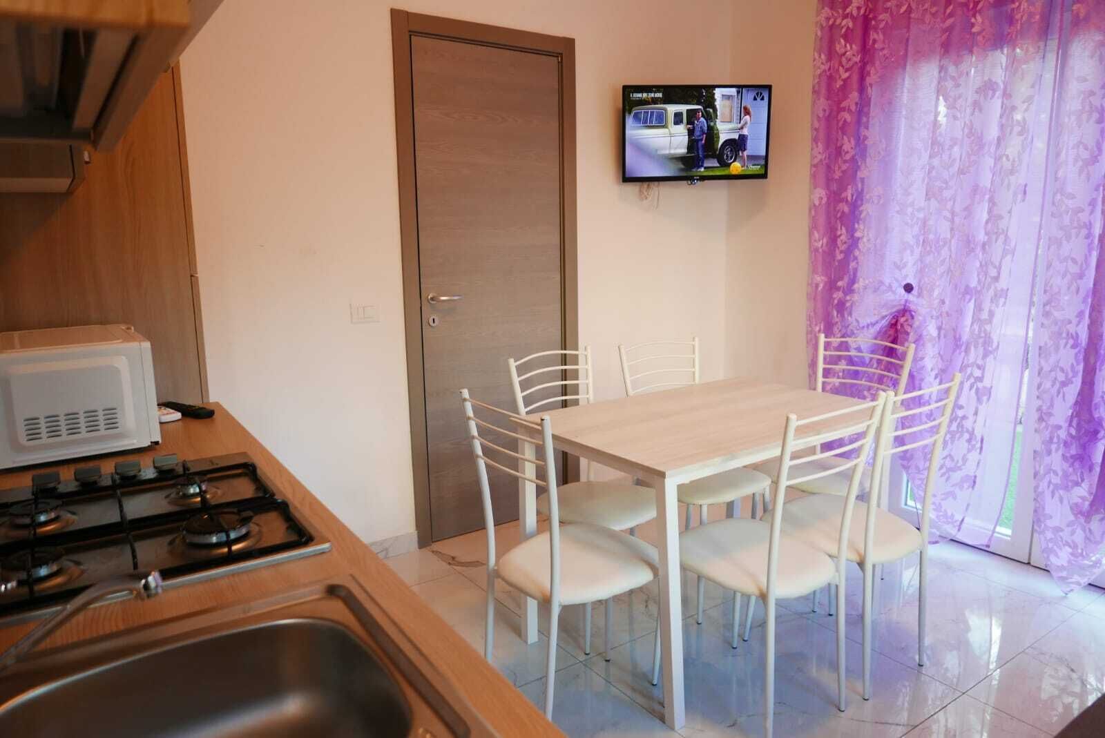 Una cocina pequeña con estufa, microondas y pileta. Hay una mesa de comedor con cuatro sillas y un televisor colocado en la pared.
