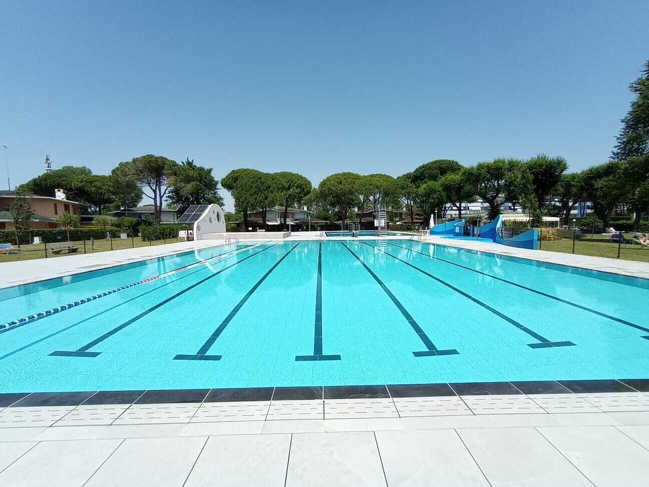 A swimming pool with clear lanes, surrounded by a tiled deck and trees.
