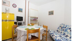 A compact room with a dining table, chairs, a yellow refrigerator, a microwave, a television, and a sofa with a floral cover. - Appartamenti Olimpia (San Michele al Tagliamento)