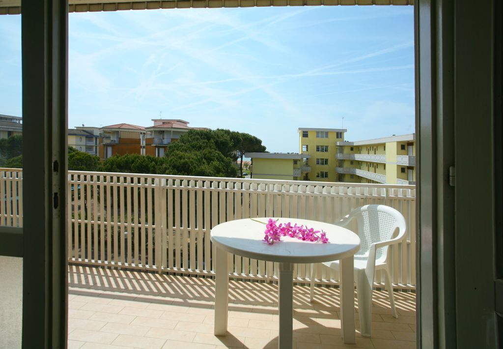 Ein Balkon mit einem weißen Tisch und Stuhl, einem weißen Zaun und Gebäuden im Hintergrund.