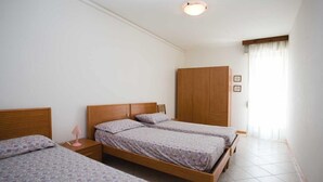 A room with two single beds, a wooden wardrobe, and a bedside table with a lamp.