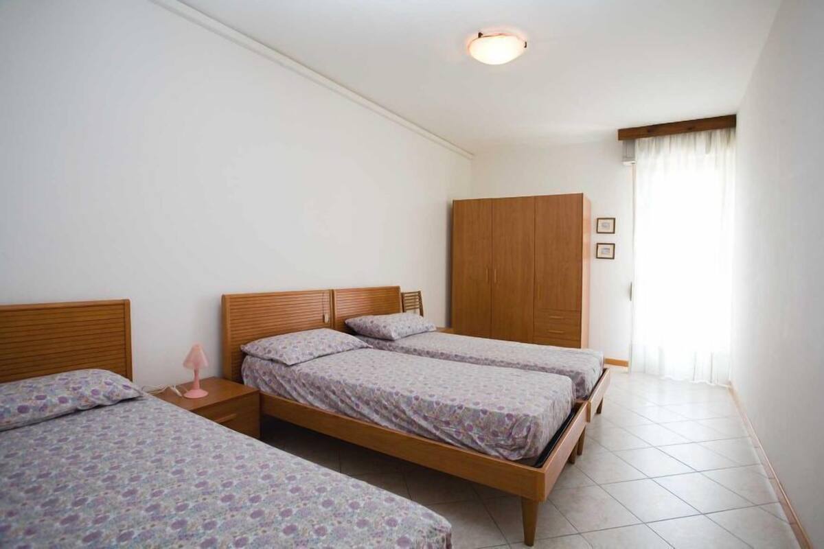 A room with two single beds, a wooden wardrobe, and a bedside table with a lamp.