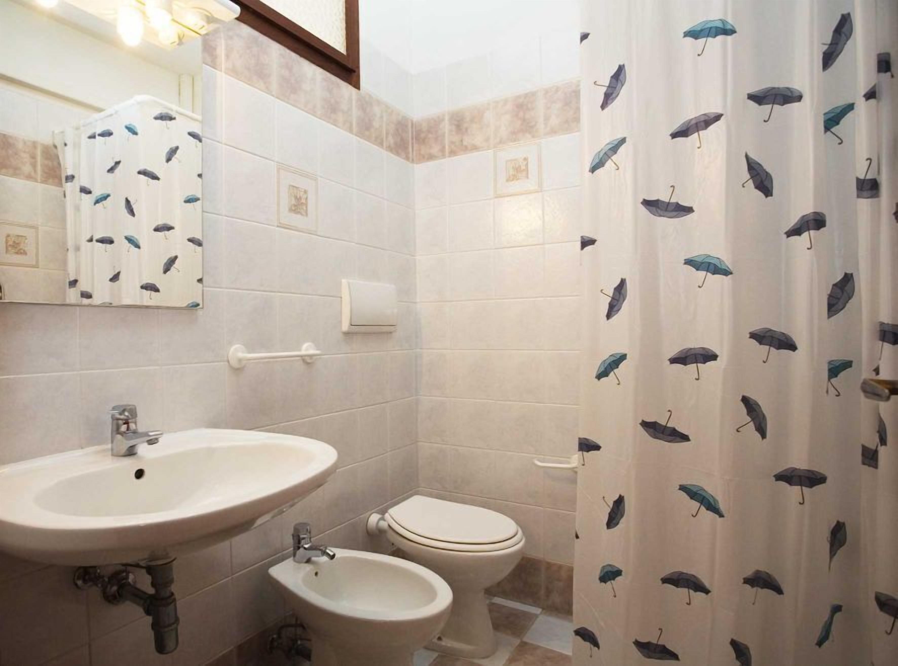 Une salle de bain équipée d’un lavabo, d’un bidet, de toilettes et d’un rideau de douche orné d’un motif de parapluies.