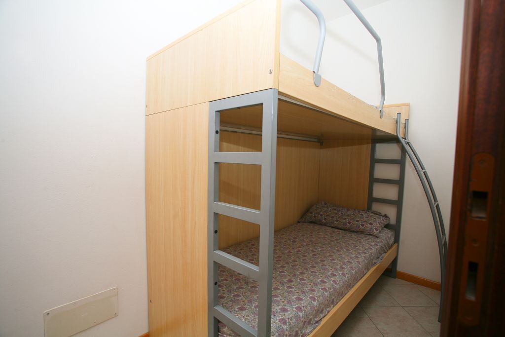 A bunk bed with a ladder, a mattress with a patterned cover, and a wooden headboard.