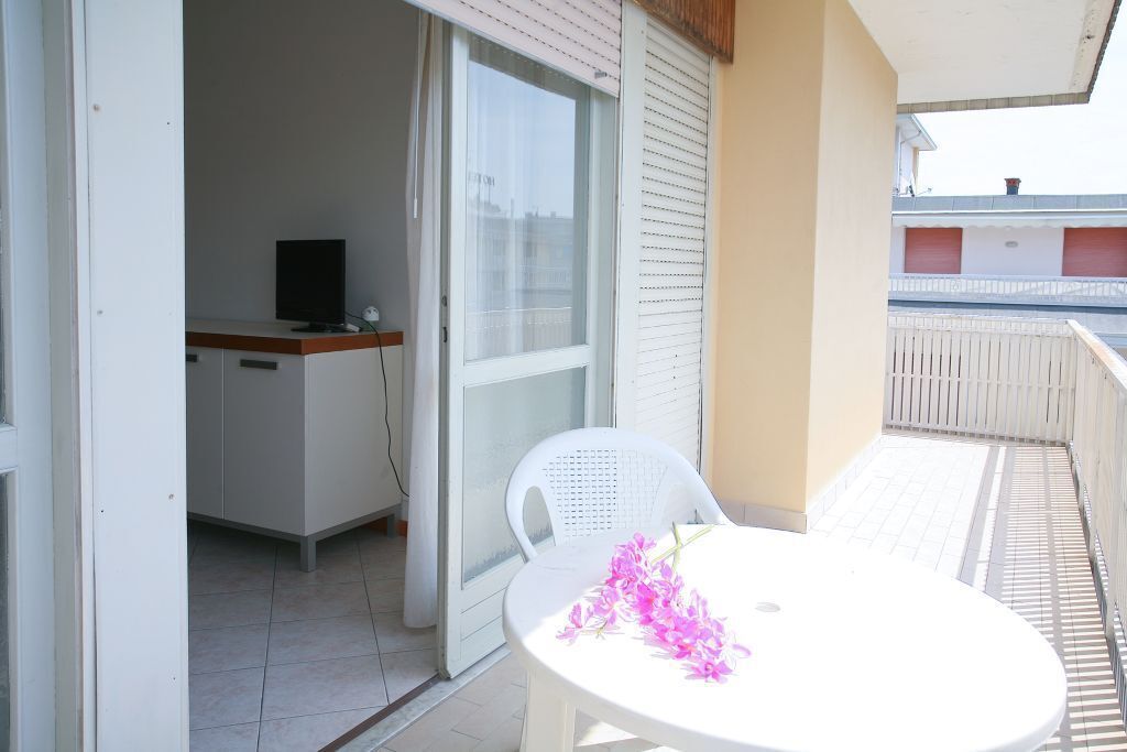 A balcony with a white table and chair, a TV on a cabinet, and a view of buildings in the background.