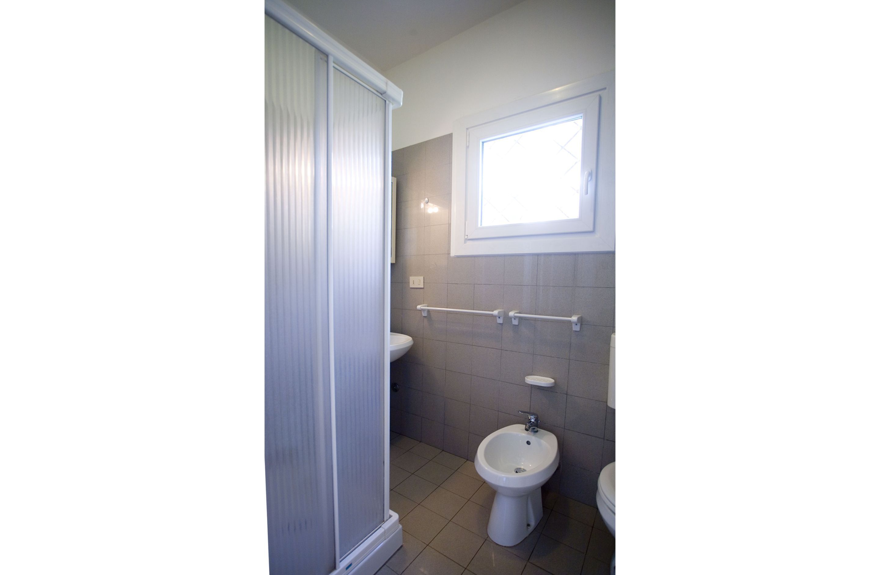 A bathroom with a toilet, bidet, and a window above the sink.