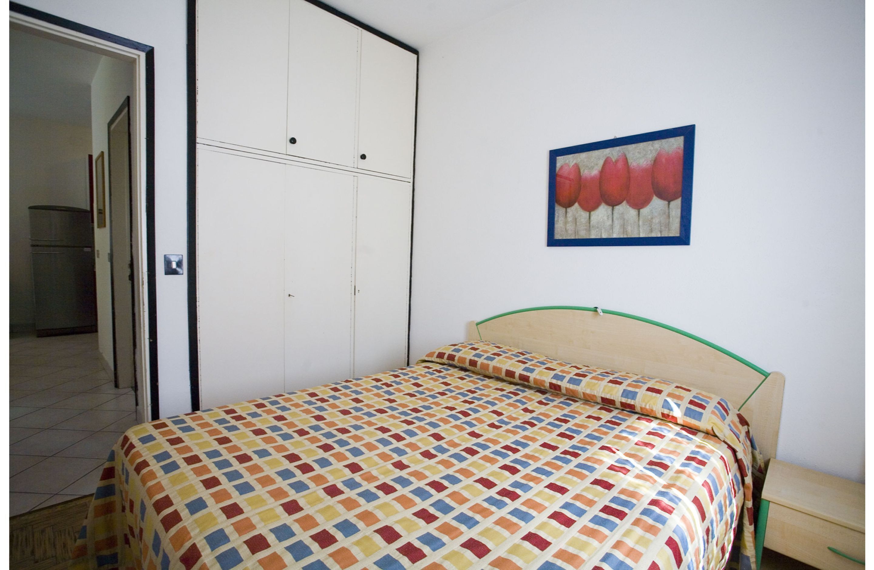 A bedroom with a bed, a wardrobe, and a picture on the wall.