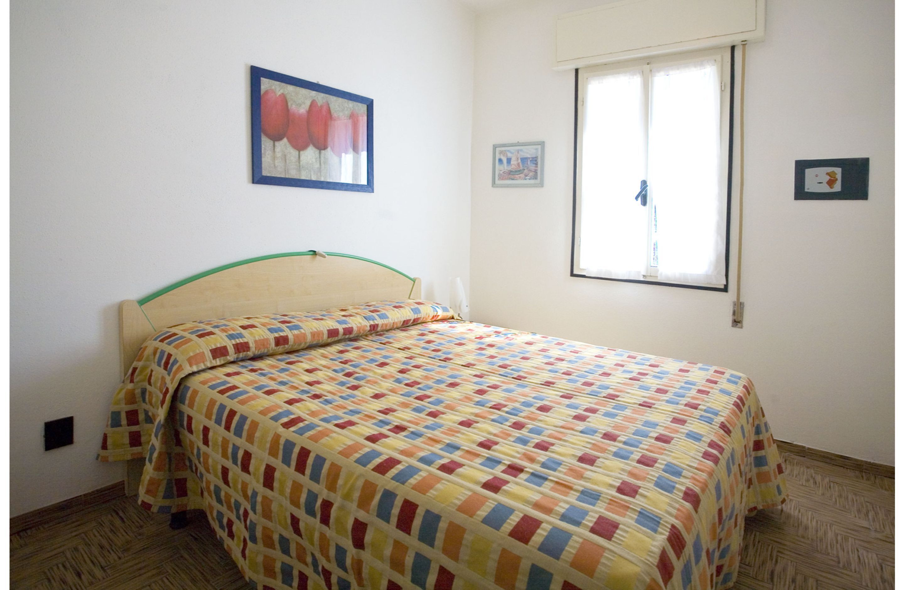 A room with a bed, a window with blinds, and two framed pictures on the wall.