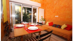 A dining area with a table set for two, a sofa with cushions, and a view through a glass door. - Villa Polluce (San Michele al Tagliamento)