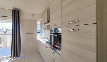 A modern kitchen with light wood cabinetry, stainless steel appliances, and a view of the outdoors.