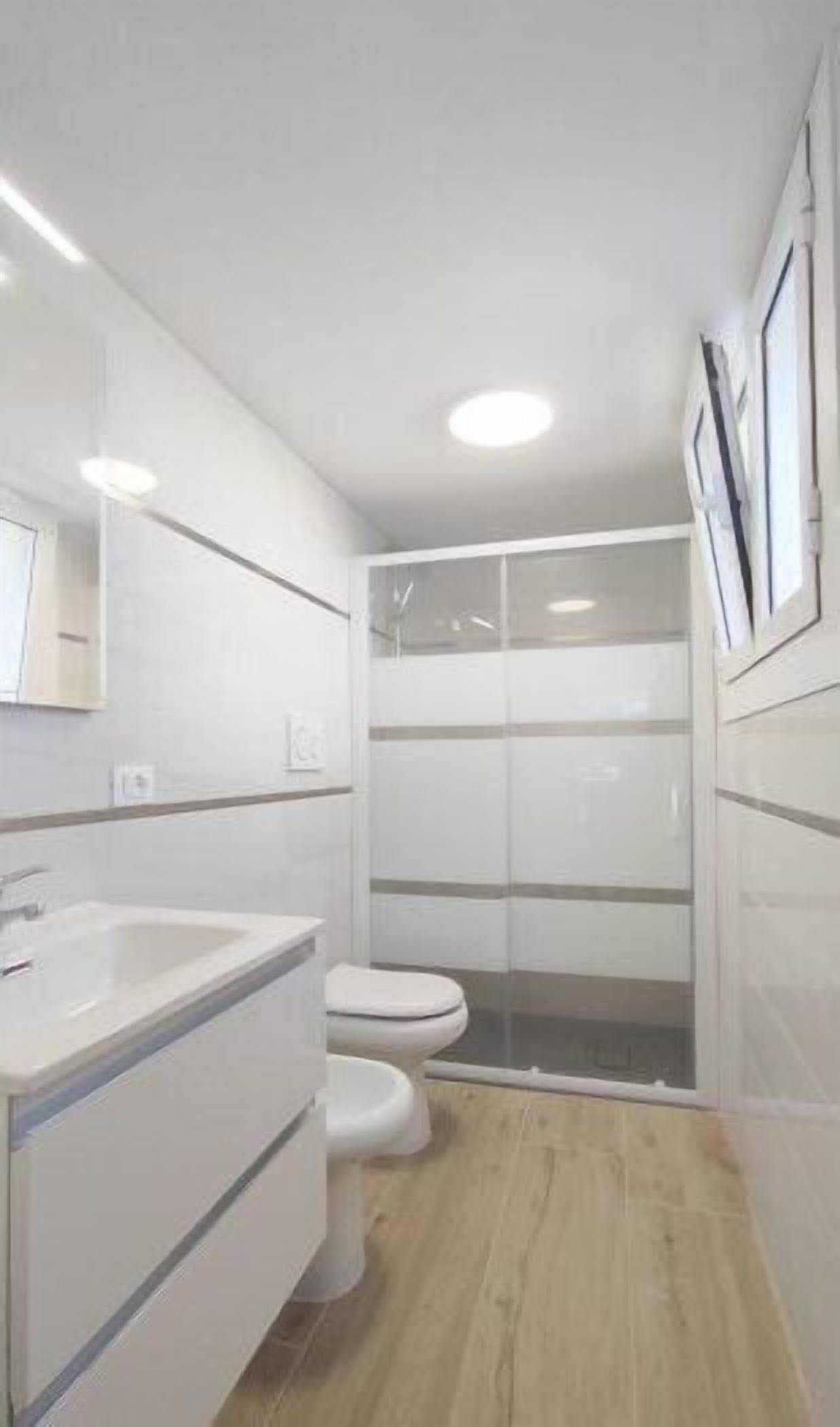 A modern bathroom with a white sink, toilet, and glass shower enclosure.
