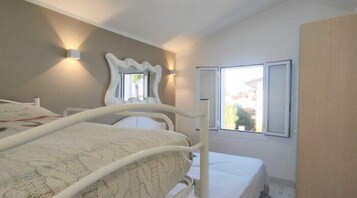 Una camera da letto con un letto, un comodino, uno specchio e una finestra che si affaccia su edifici.