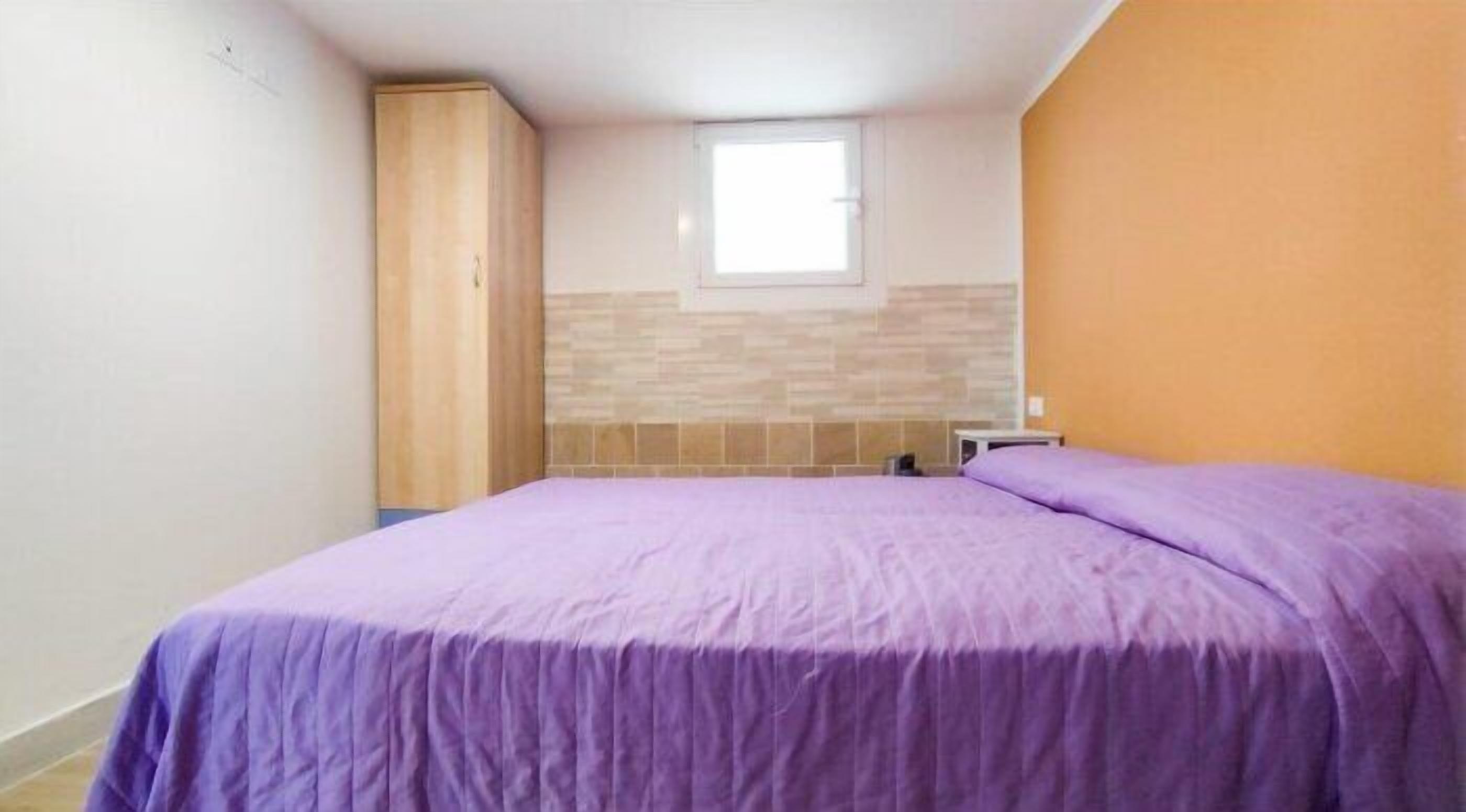 A bedroom with a bed, a wardrobe, a window, and a tiled wall.