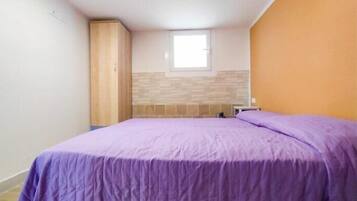 A bedroom with a bed, a wardrobe, a window, and a tiled wall.