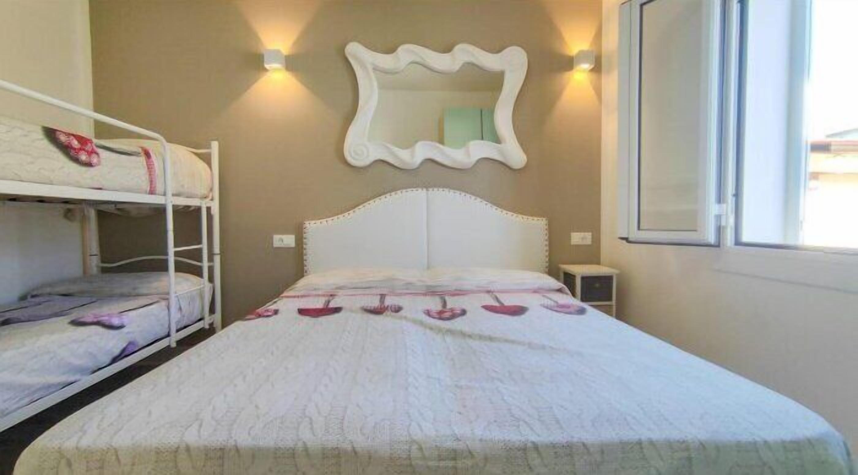 A single bed with a white headboard, a bunk bed to the left, and a wall-mounted mirror above.