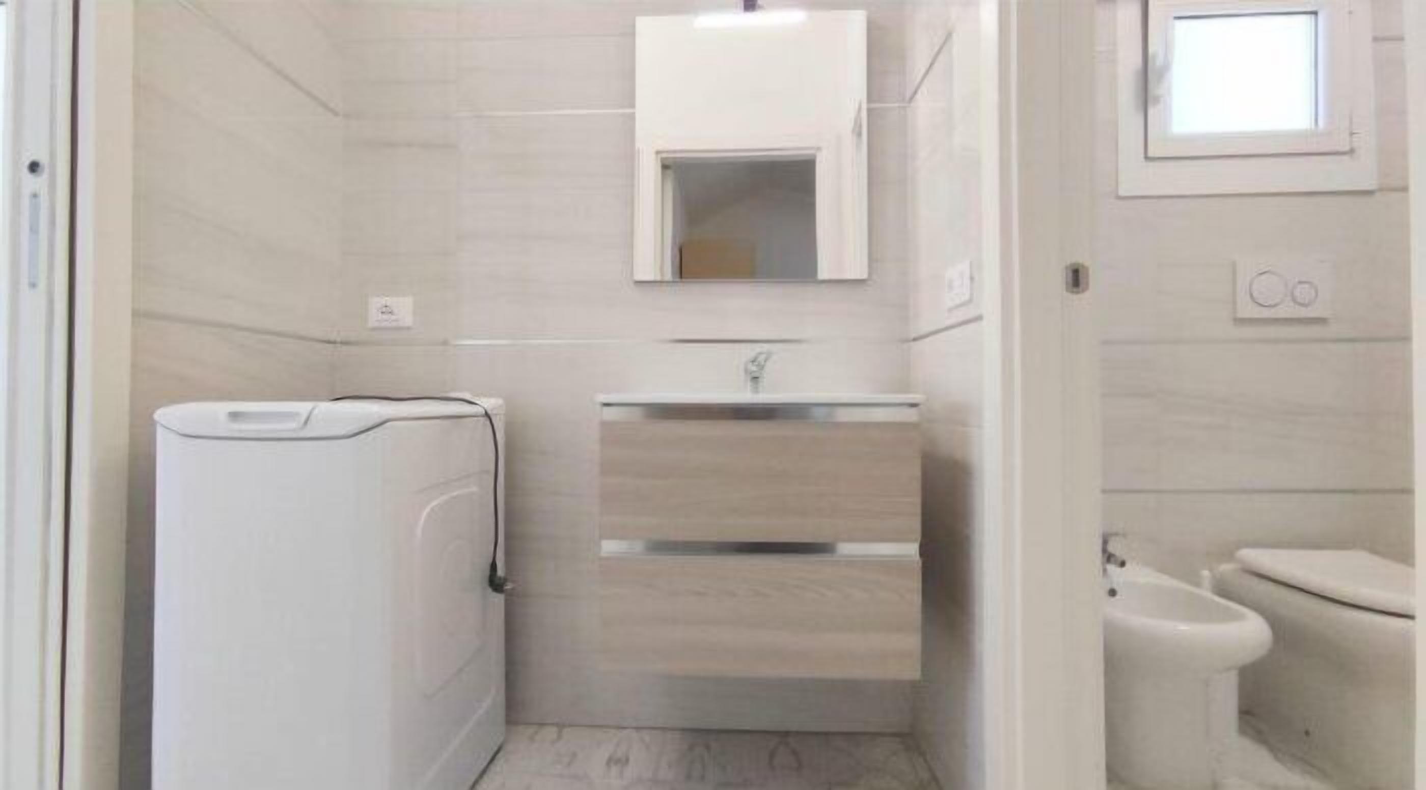 A small, compact bathroom with a built-in washer and dryer, a mirror above the sink, and a toilet.