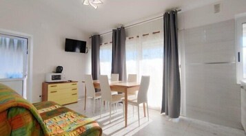 Una camera con un letto, una scrivania con un computer, un televisore montato a parete e un'area pranzo con sedie e tavolo.