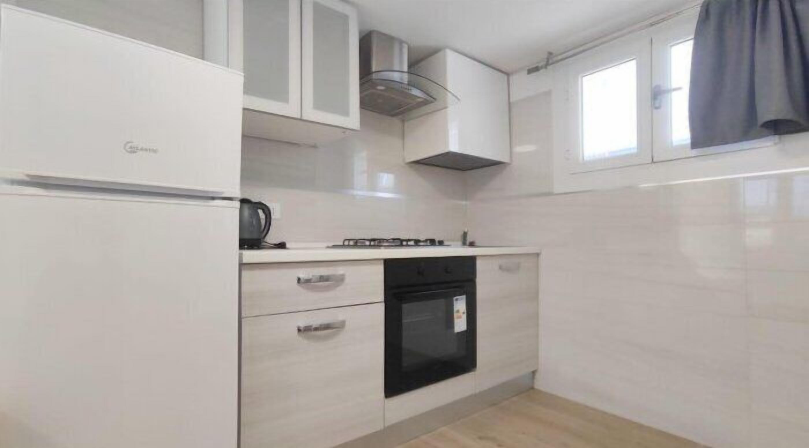 Cozinha compacta com armários brancos, fogão e forno preto.