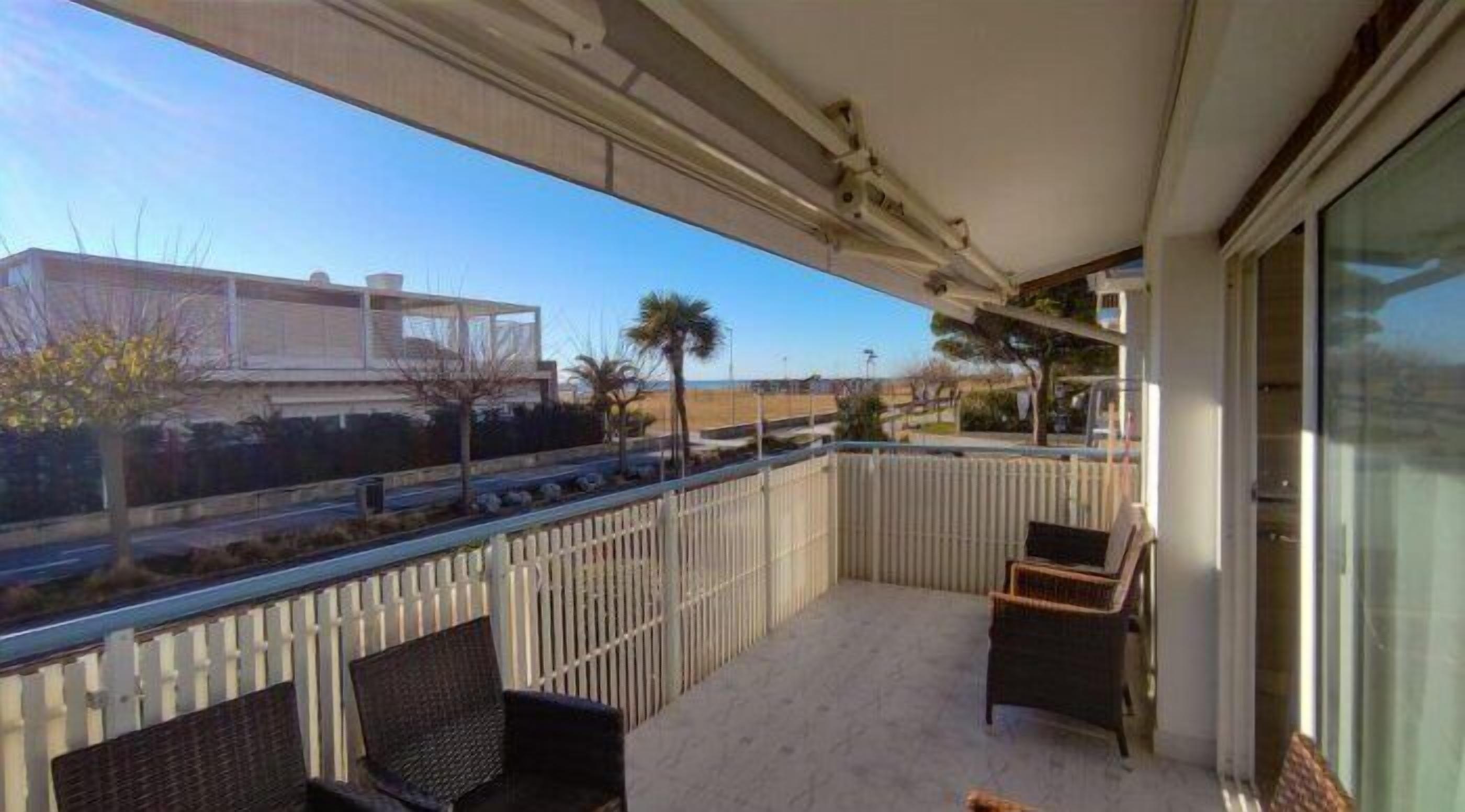 Ein Balkon mit zwei Korbstühlen, Blick auf einen Strand und ein Gebäude im Hintergrund.
