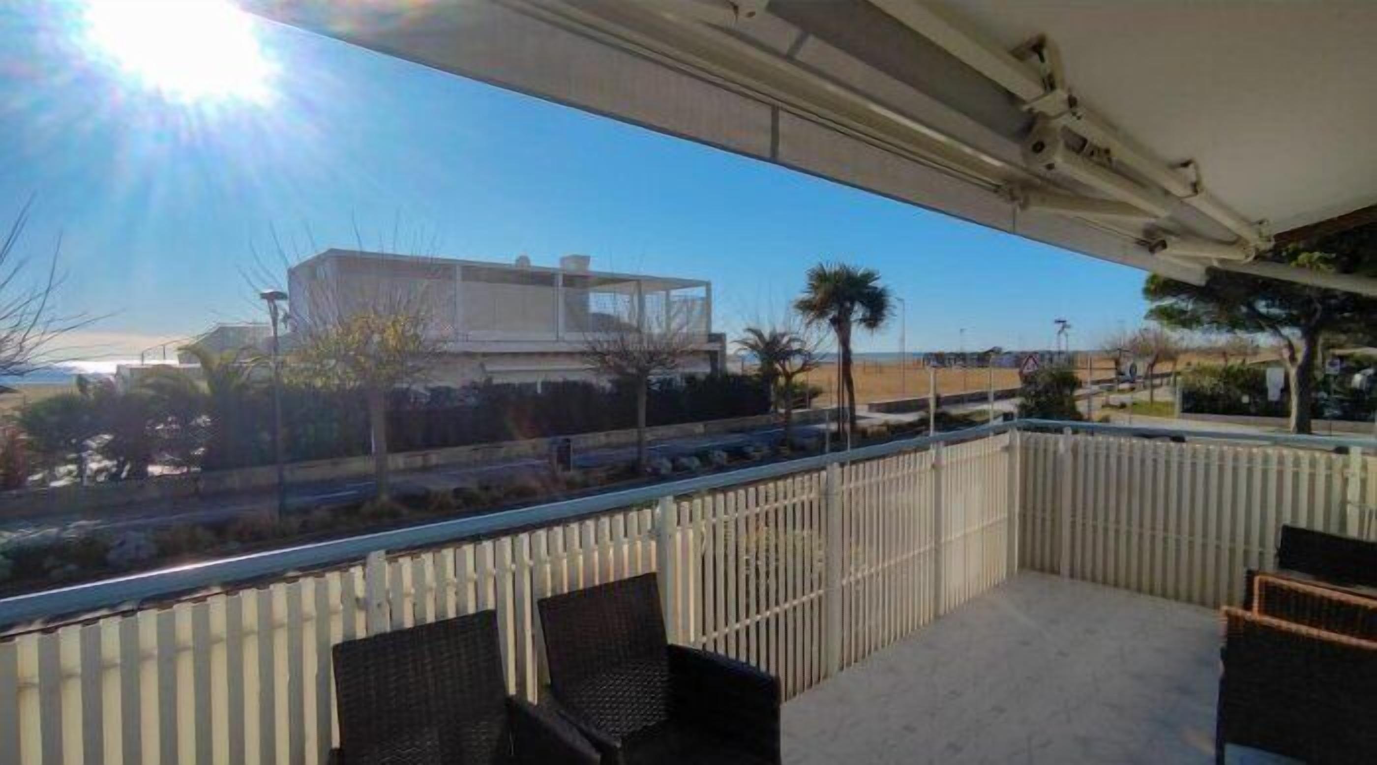 A balcony with a view of a modern building, palm trees, and a beach.