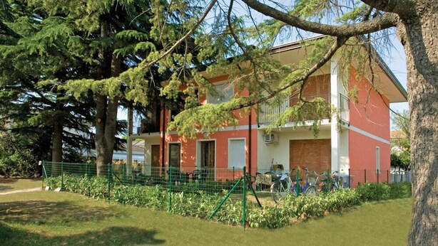 A red building with a balcony, surrounded by greenery and trees.