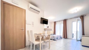 Une chambre d’hôtel équipée d’une table à manger, de chaises, d’un lit avec une couvre-lit à motifs, d’un téléviseur fixé au mur et d’une porte-fenêtre coulissante donnant sur un espace extérieur.