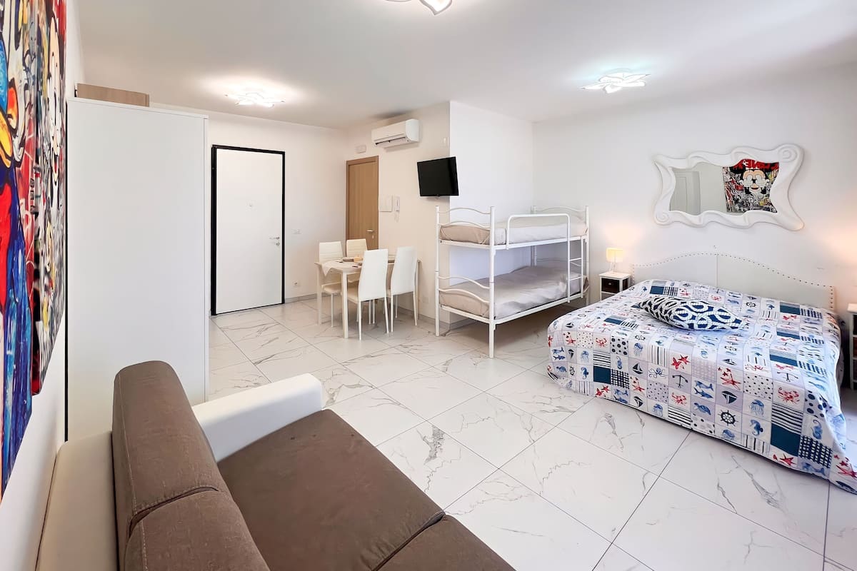 Een kamer met een stapelbed, een slaapbank, een eettafel met stoelen en een aan de muur bevestigde televisie.