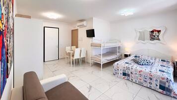A room with a bunk bed, a sofa, a dining table with chairs, and a TV mounted on the wall.