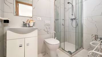 A modern bathroom with a glass-enclosed shower, a white sink, and a toilet.