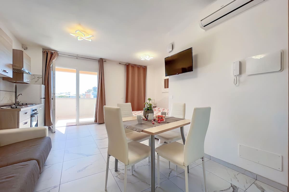 Een moderne keuken met een ingebouwde kookplaat, een eethoek met een tafel en stoelen, en een aan de muur bevestigde televisie.