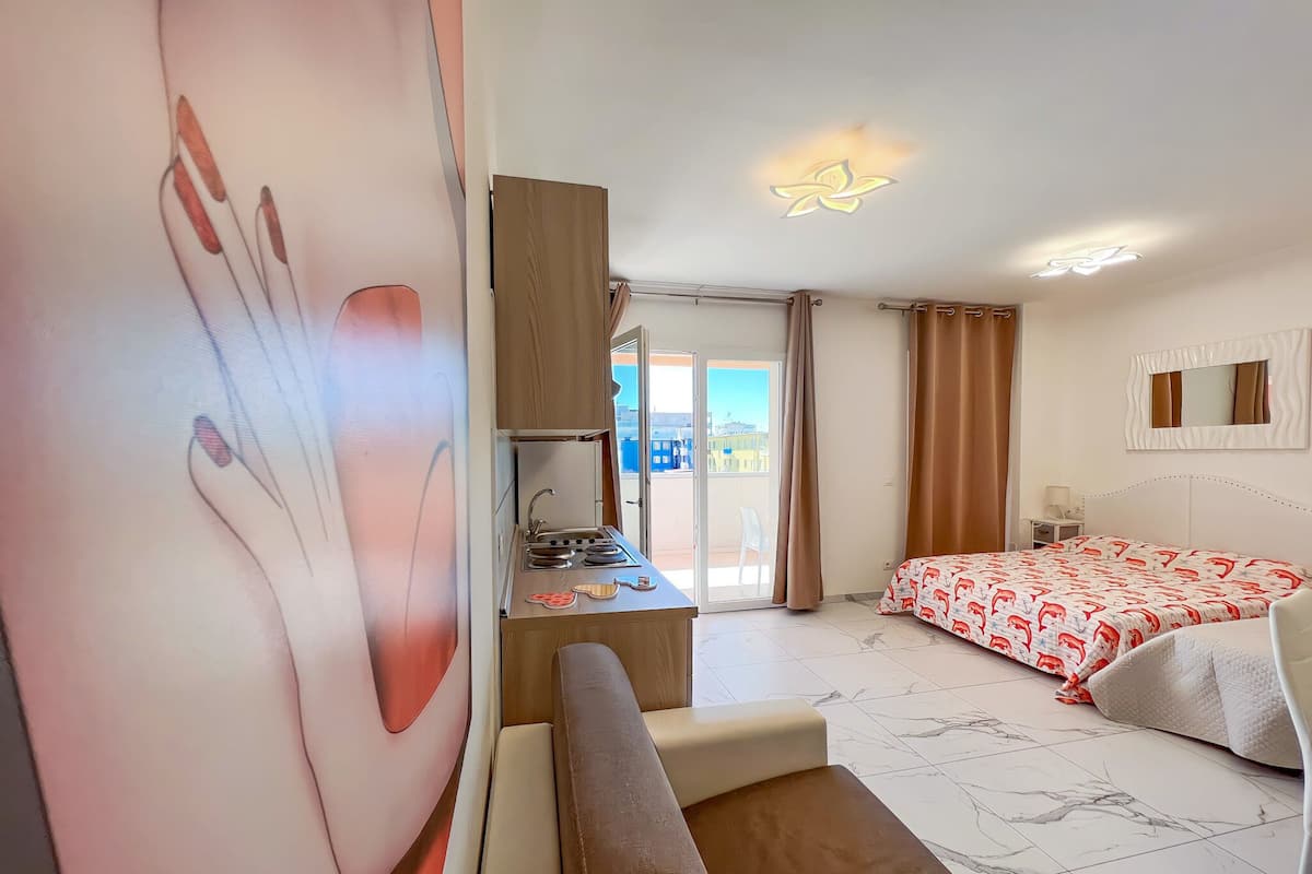 Een hotelkamer met een bed, een bank, een bureau met een wastafel en een balkon met uitzicht op gebouwen.