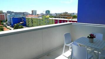A balcony with white chairs and a table, overlooking a cityscape with colorful buildings.