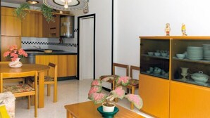 A compact kitchen with wooden cabinets, a dining table with chairs, and a cabinet with dishes. - Appartamenti Tiziano (San Michele al Tagliamento)
