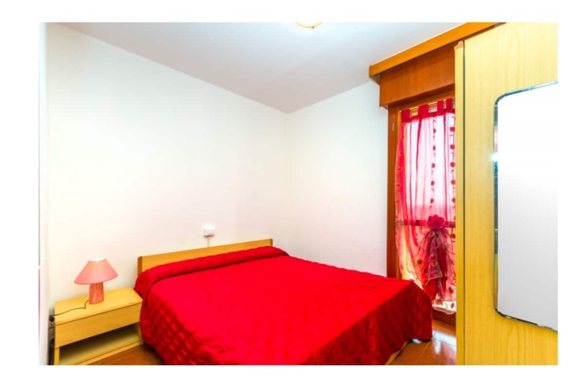 Un dormitorio con una cama individual, una mesita de noche, una lámpara y un ventanal con cortinas.
