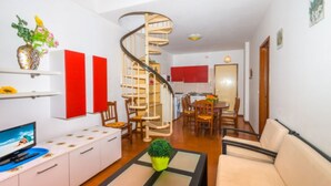 Un salon moderne avec un escalier en colimaçon, un téléviseur, un canapé et un coin repas.