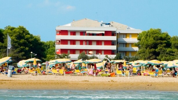 Une plage avec des parasols aux couleurs vives et, en arrière-plan, un immeuble à plusieurs étages.