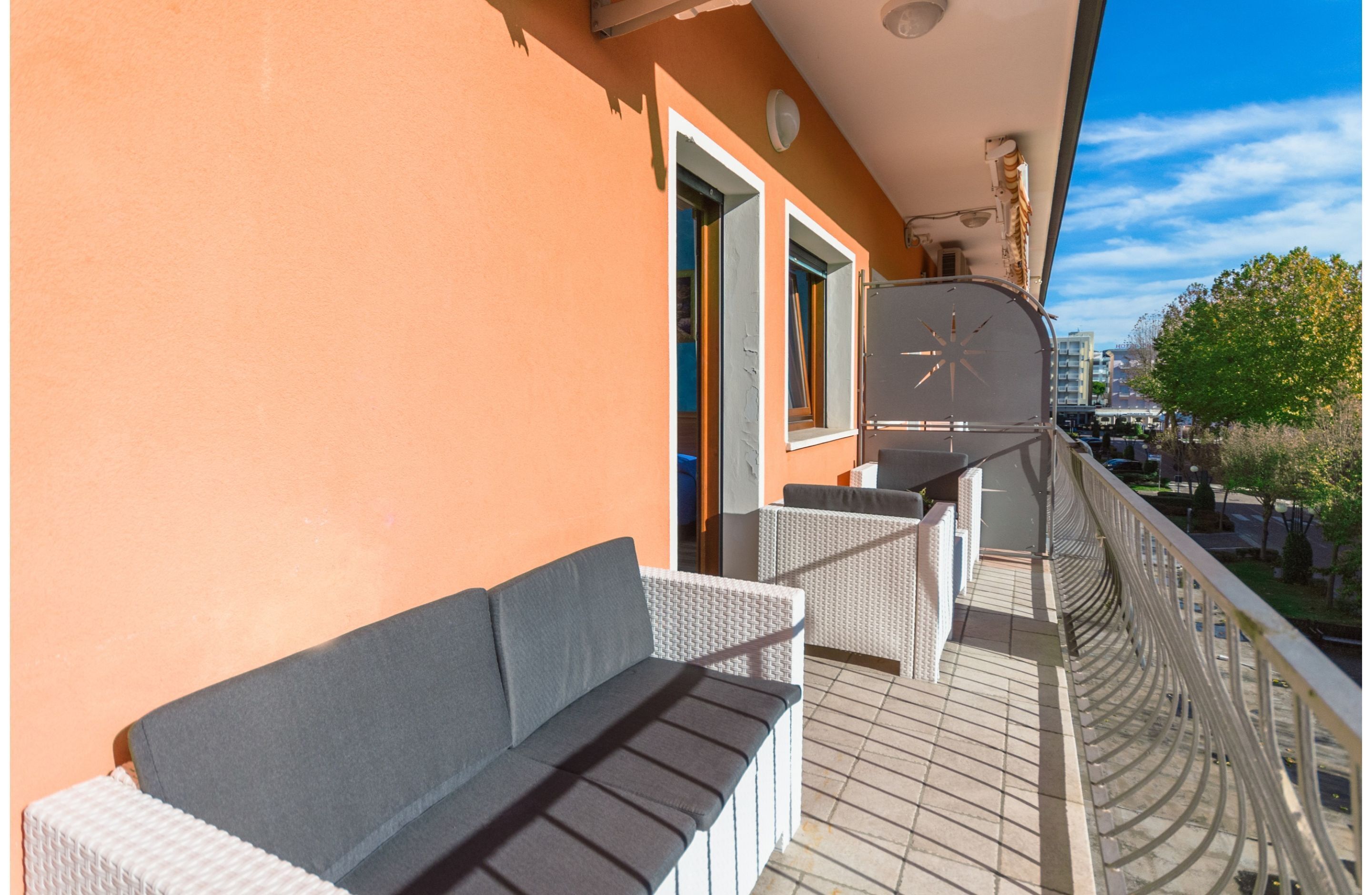 A balcony with wicker furniture, a view of the street, and a building in the background.